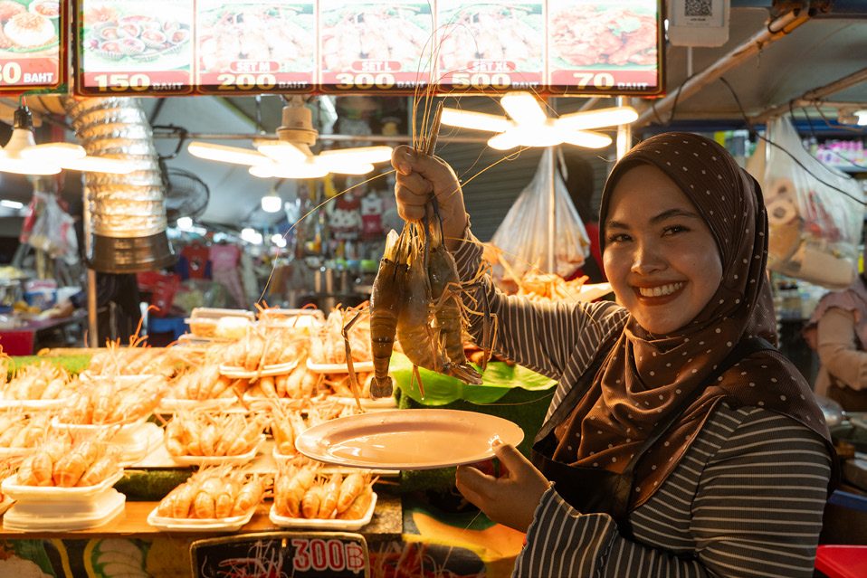 Smiling vendor holding a plate of fried seafood at a night market in Hat Yai